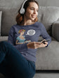Woman sitting on a couch wearing a purple sweatshirt with graphic designs, using a phone.