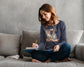 Woman sitting on a couch, writing in a notebook with a gray wall background