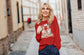 Woman wearing a red sweatshirt with graphic design, standing in an urban setting.