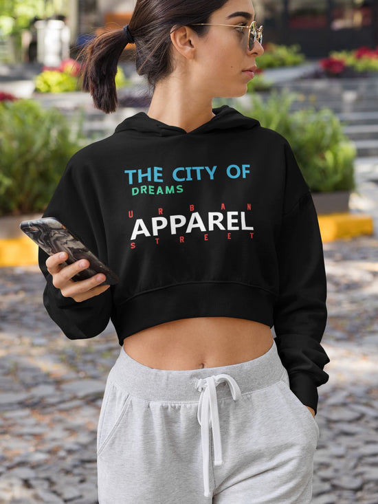 Woman wearing a black hoodie with text, holding a phone, standing outdoors.