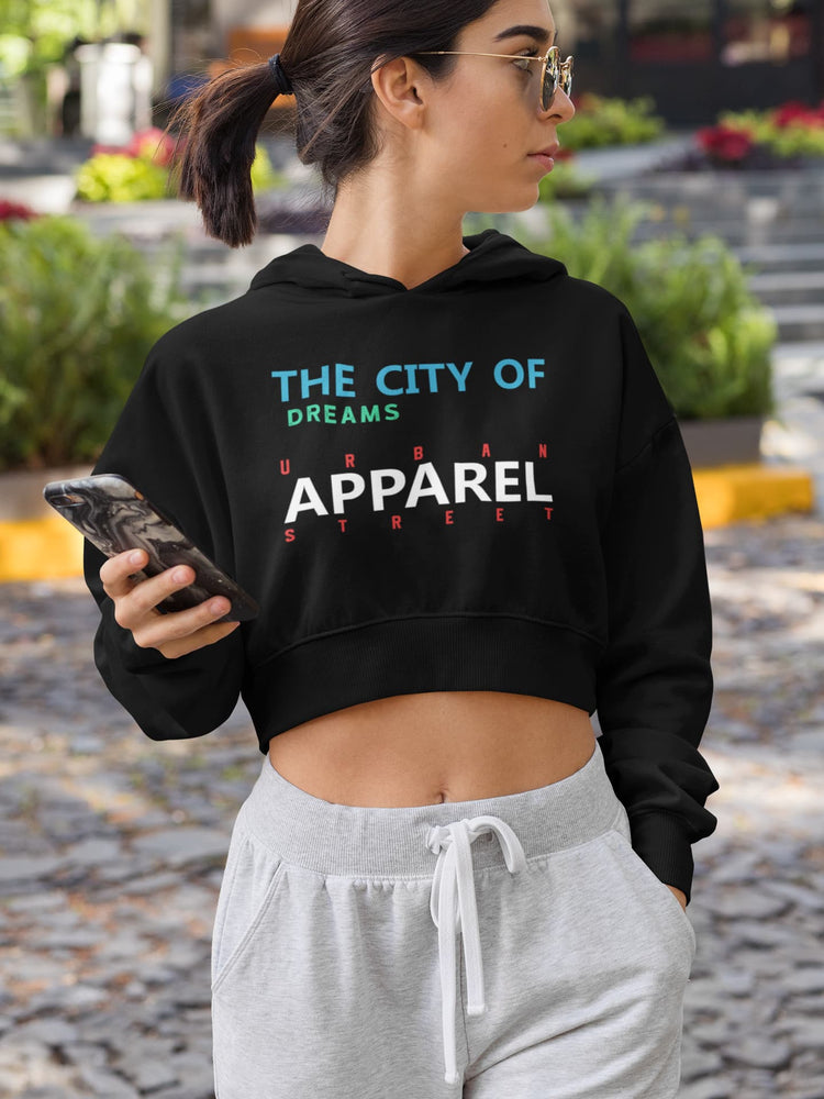 Woman wearing a black hoodie with text, holding a phone, standing outdoors.