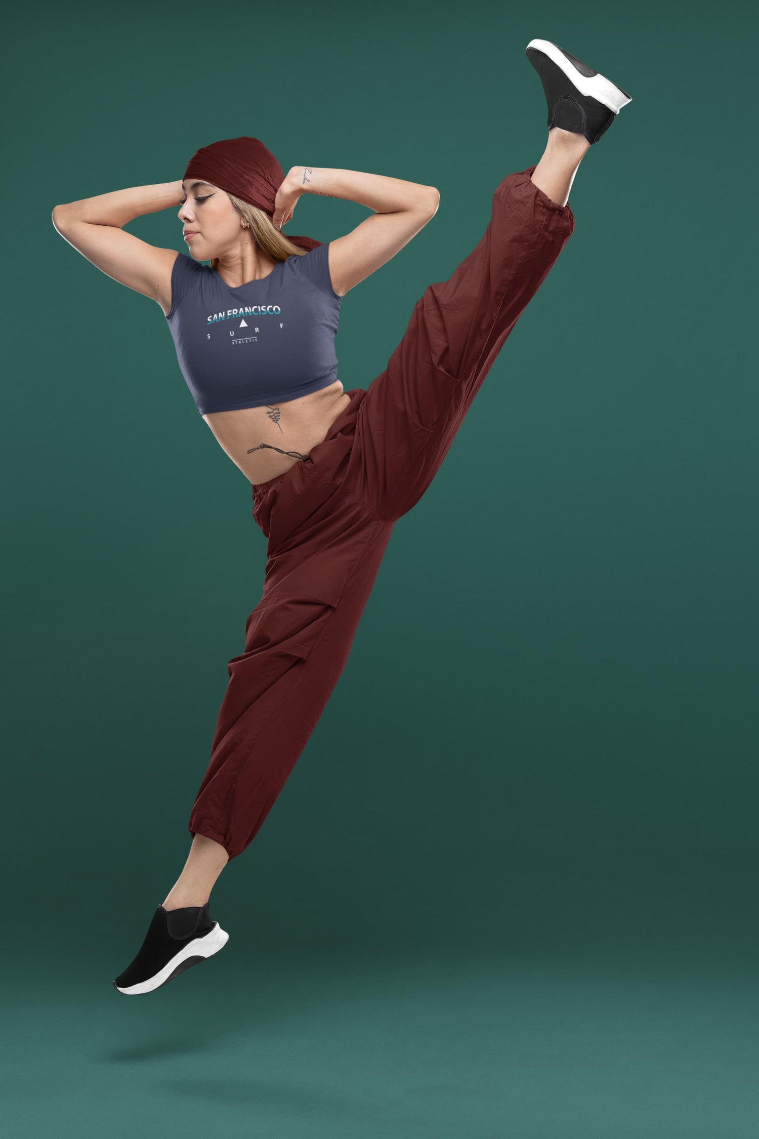 Person in maroon pants and gray tank top posing against a green background