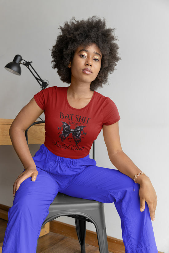 Person wearing a red t-shirt with a graphic design and blue pants sitting on a chair.