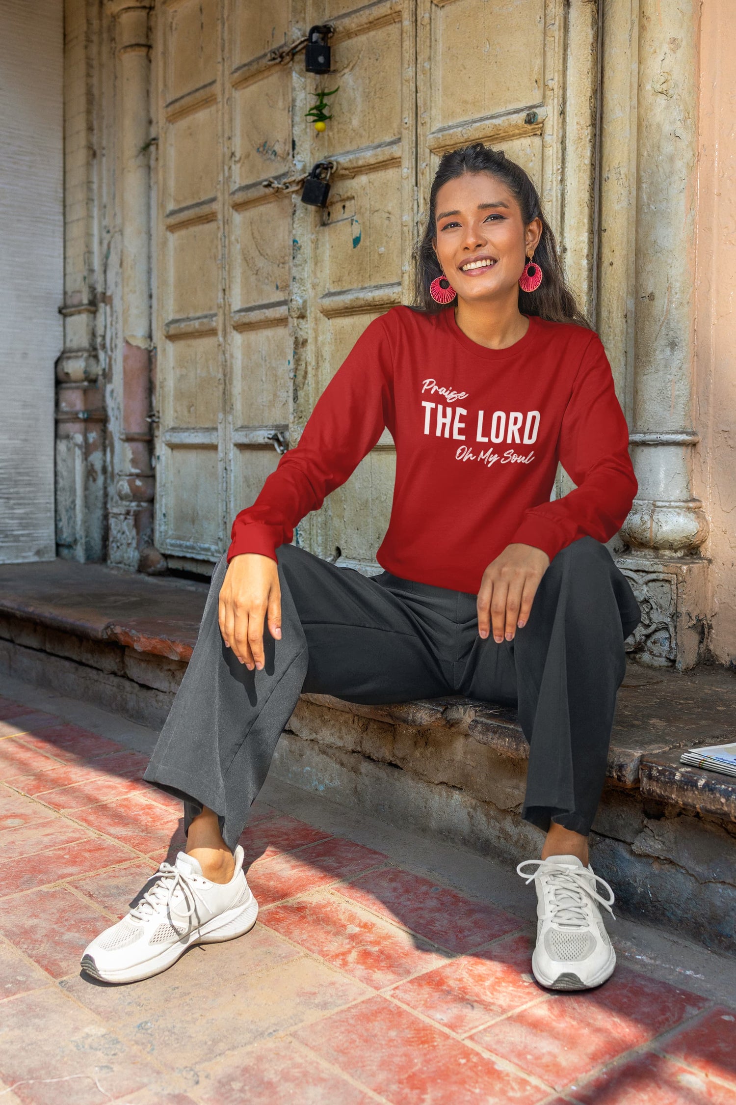 Woman wearing a red sweatshirt with text, sitting on steps.