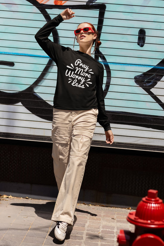 Person wearing a black sweatshirt with text, beige pants, and red sunglasses in an urban setting.