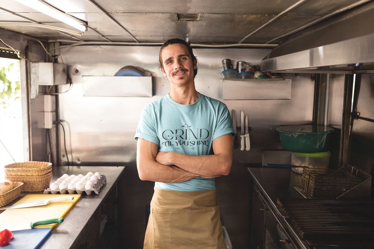 Man standing in a kitchen wearing a 'Grind Til You Drop' t-shirt.