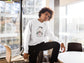 Person wearing a white sweatshirt with a design, sitting in a modern office setting.