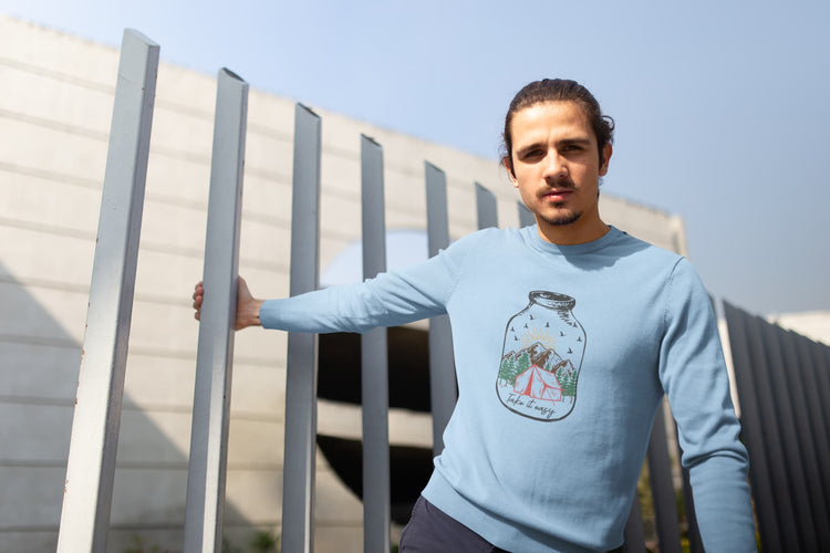 Man wearing a light blue sweater with a design, standing outdoors.
