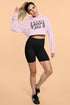 Woman wearing a pink hoodie with text and black shorts on a beige background