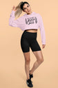 Woman wearing a pink hoodie with text and black shorts on a beige background