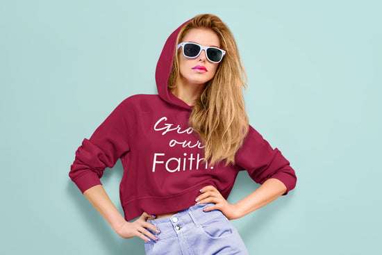 Woman wearing a maroon hoodie with text, sunglasses, and light blue pants on a light blue background