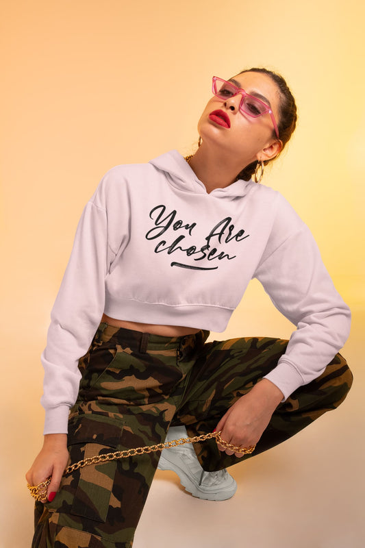Woman wearing a white hoodie with 'You Are Chosen' text and camouflage pants on a beige background