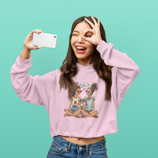 Woman wearing a pink sweatshirt with a graphic design, taking a selfie against a teal background