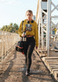 Person walking on a bridge wearing a yellow hoodie with a graphic design, holding a water bottle and a bag.