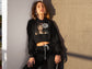 Woman wearing a black hoodie with graphic design against a beige wall