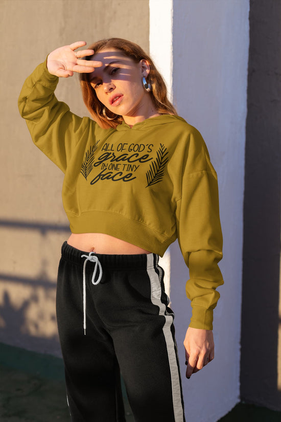Woman wearing a green sweatshirt with text and black pants against a wall.