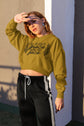 Woman wearing a green sweatshirt with text and black pants against a wall.