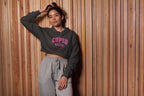 Person wearing a dark gray hoodie with 'CUPID' text and gray pants against a wooden paneled wall.