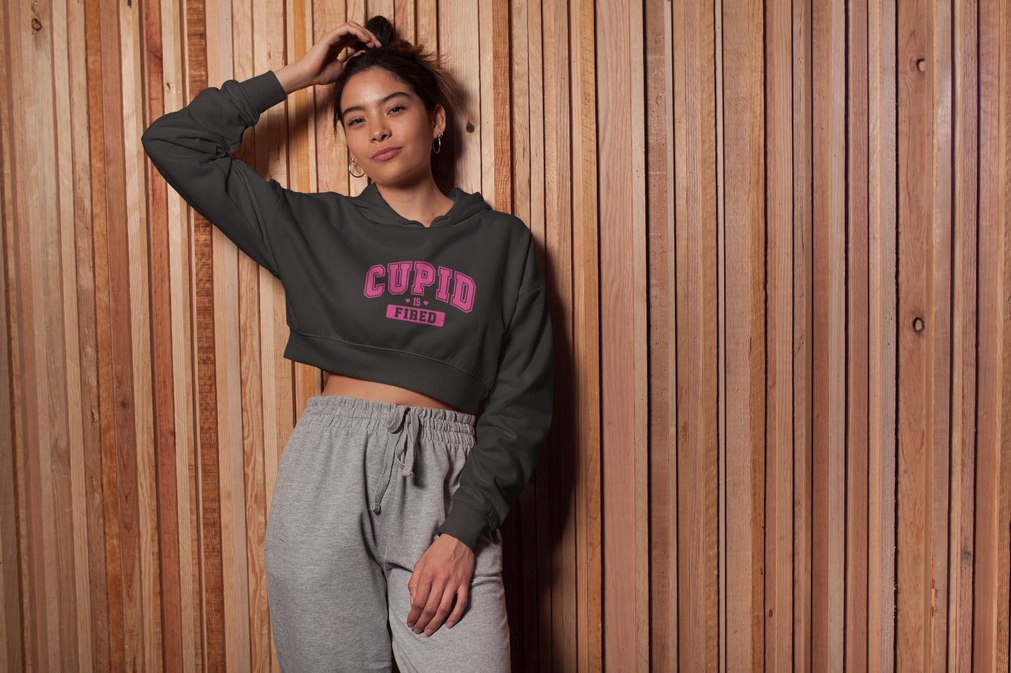 Person wearing a dark gray hoodie with 'CUPID' text and gray pants against a wooden paneled wall.