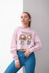 Woman wearing a pink hoodie with cartoon characters and text, standing against a gray background