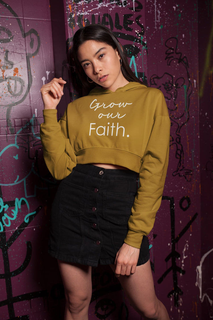 Woman wearing a mustard yellow sweatshirt with text, standing against a graffiti-covered wall.