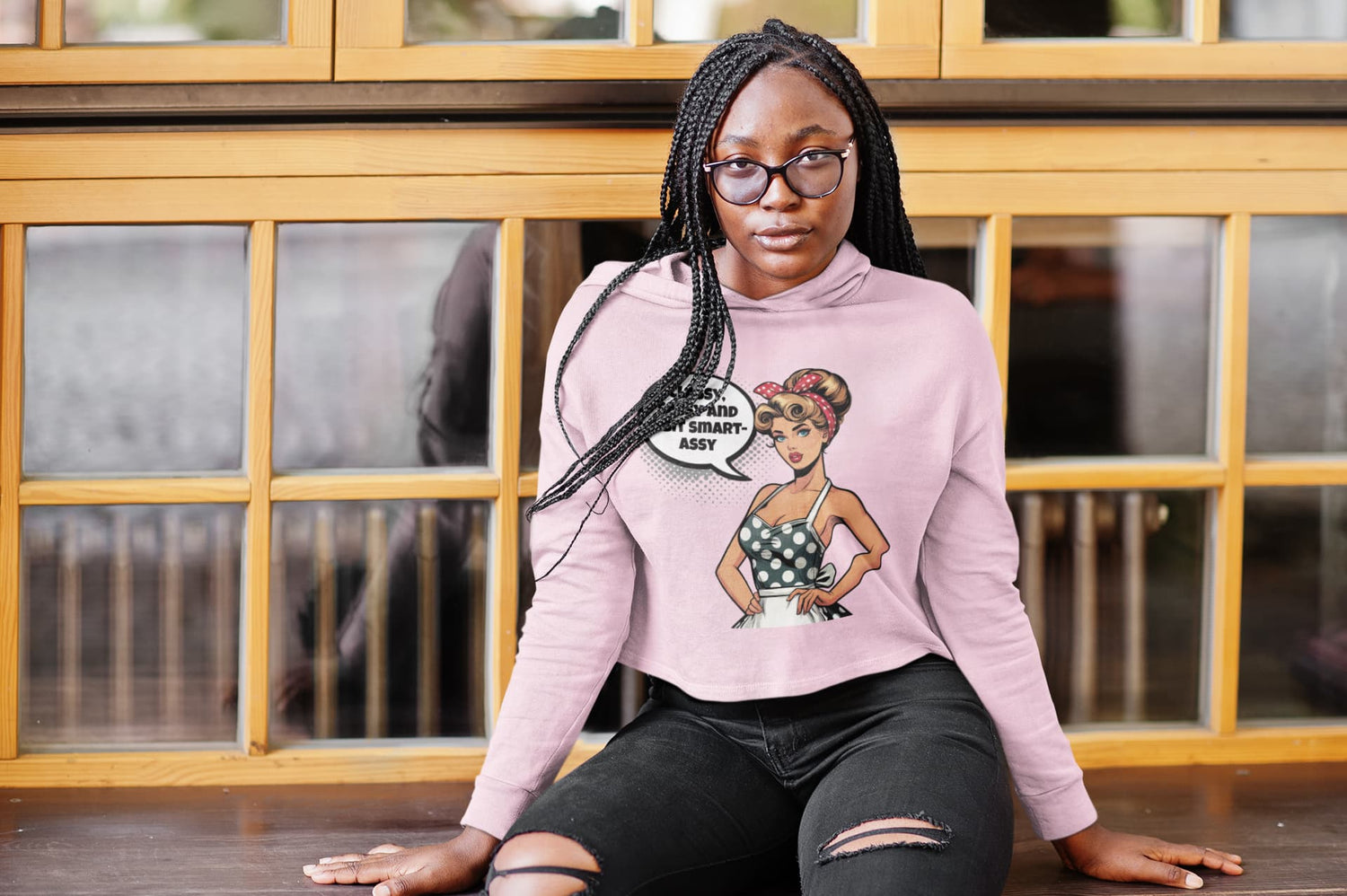 Person wearing a pink sweatshirt with a graphic design sitting in front of a wooden window.