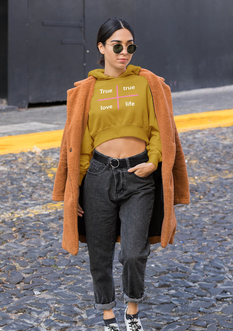 Woman wearing a mustard yellow hoodie with text, dark jeans, and an orange coat on a street.
