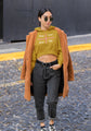 Woman wearing a mustard yellow hoodie with text, dark jeans, and an orange coat on a street.