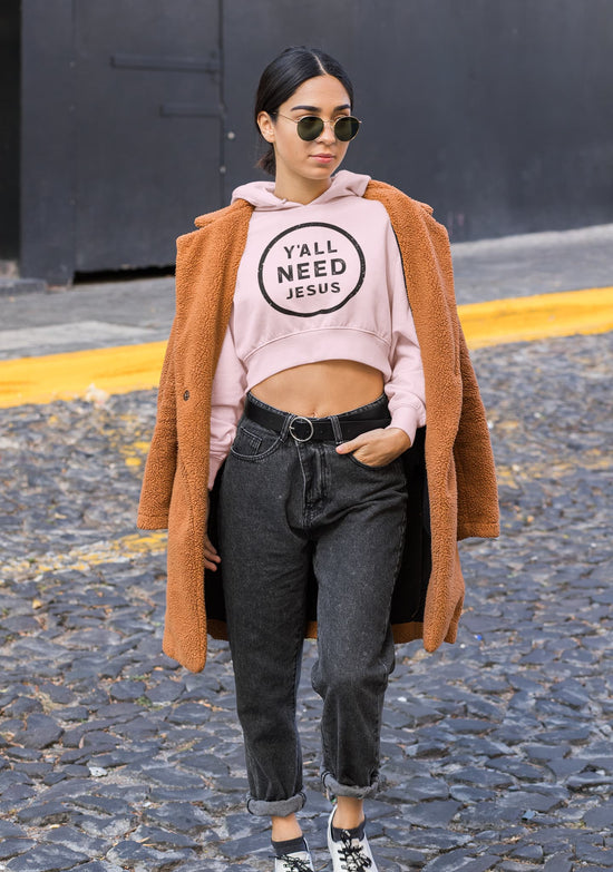 Woman wearing a pink hoodie with text, black pants, and a brown coat on a street.