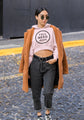 Woman wearing a pink hoodie with text, black pants, and a brown coat on a street.