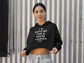 Woman wearing a black hoodie with text standing against a corrugated metal wall.