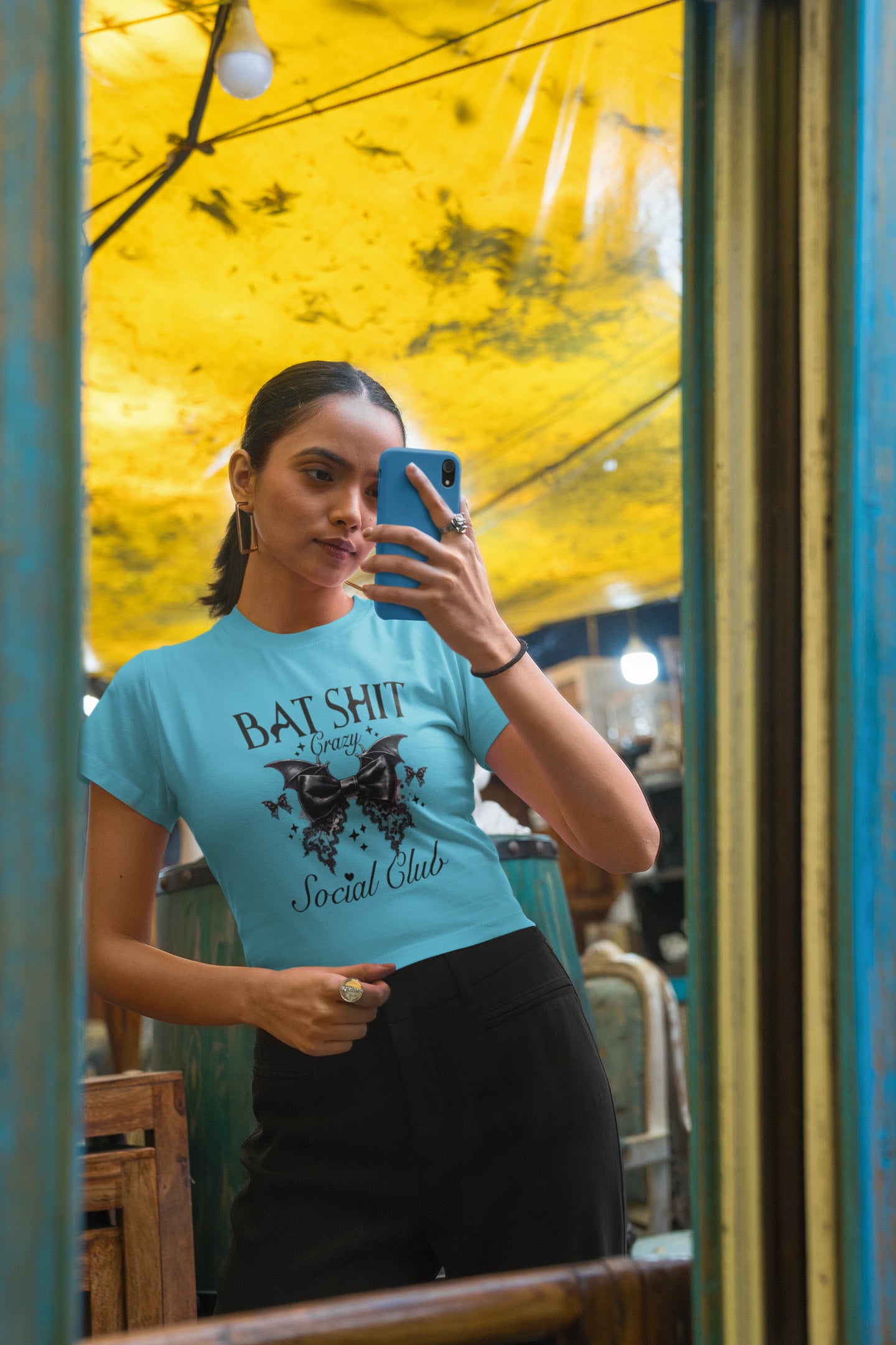Person wearing a blue t-shirt with text and a butterfly graphic, standing in front of a yellow wall.