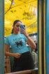 Person wearing a blue t-shirt with text and a butterfly graphic, standing in front of a yellow wall.