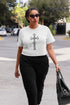 Woman walking outdoors wearing a white t-shirt with a black cross design.