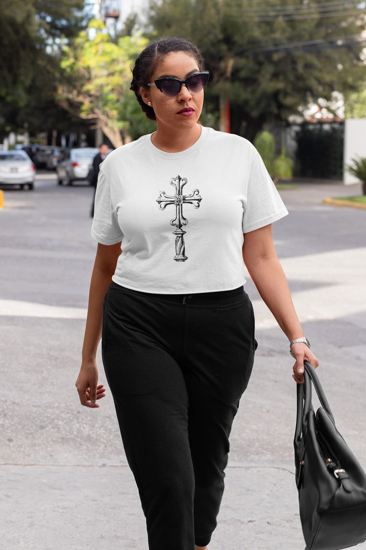 Woman walking outdoors wearing a white t-shirt with a black cross design.