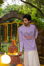 Man wearing a purple sweatshirt with text, standing outdoors with greenery and decorative archway in the background.