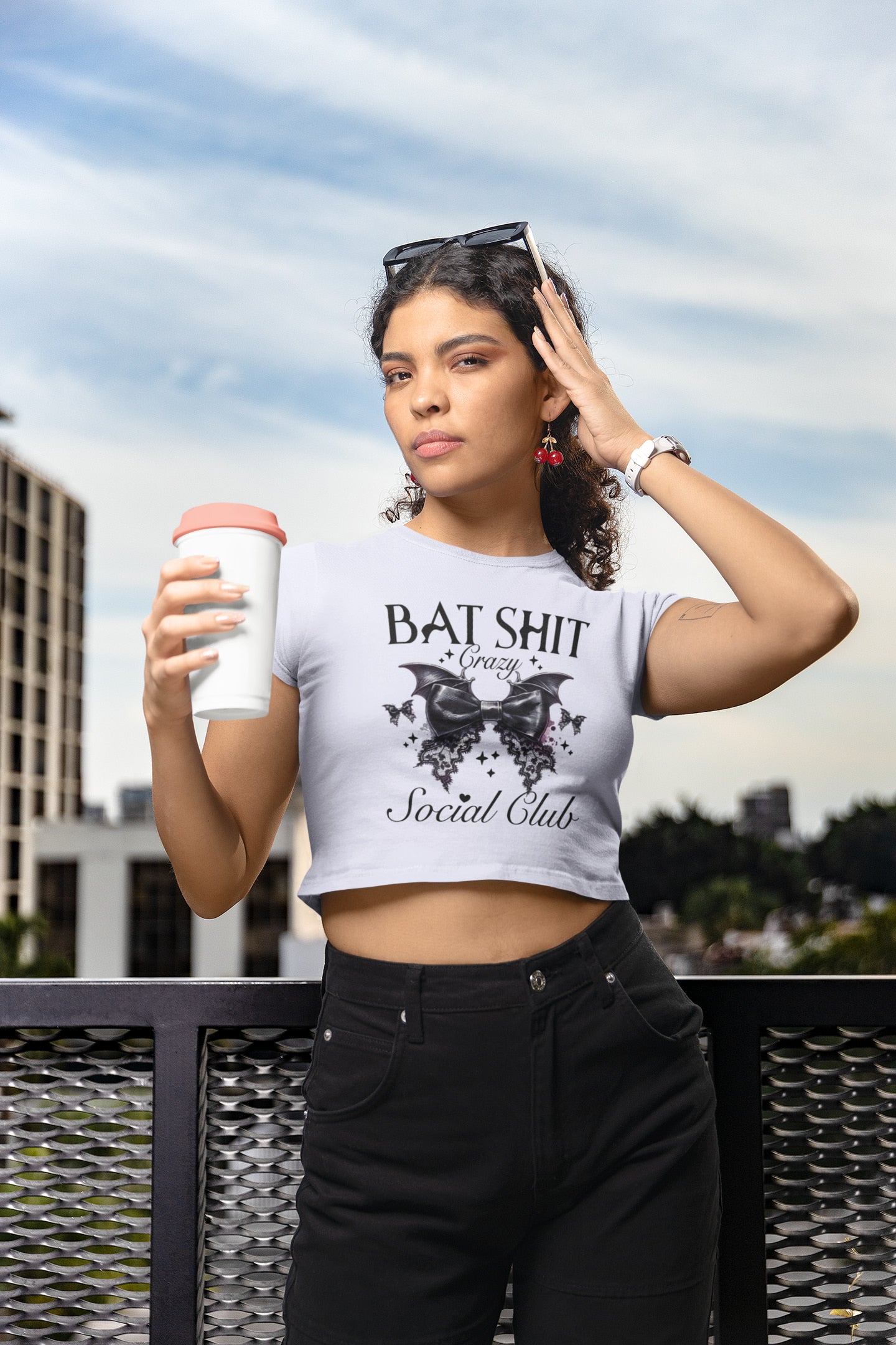 Woman holding a coffee cup with text on her shirt against an urban background