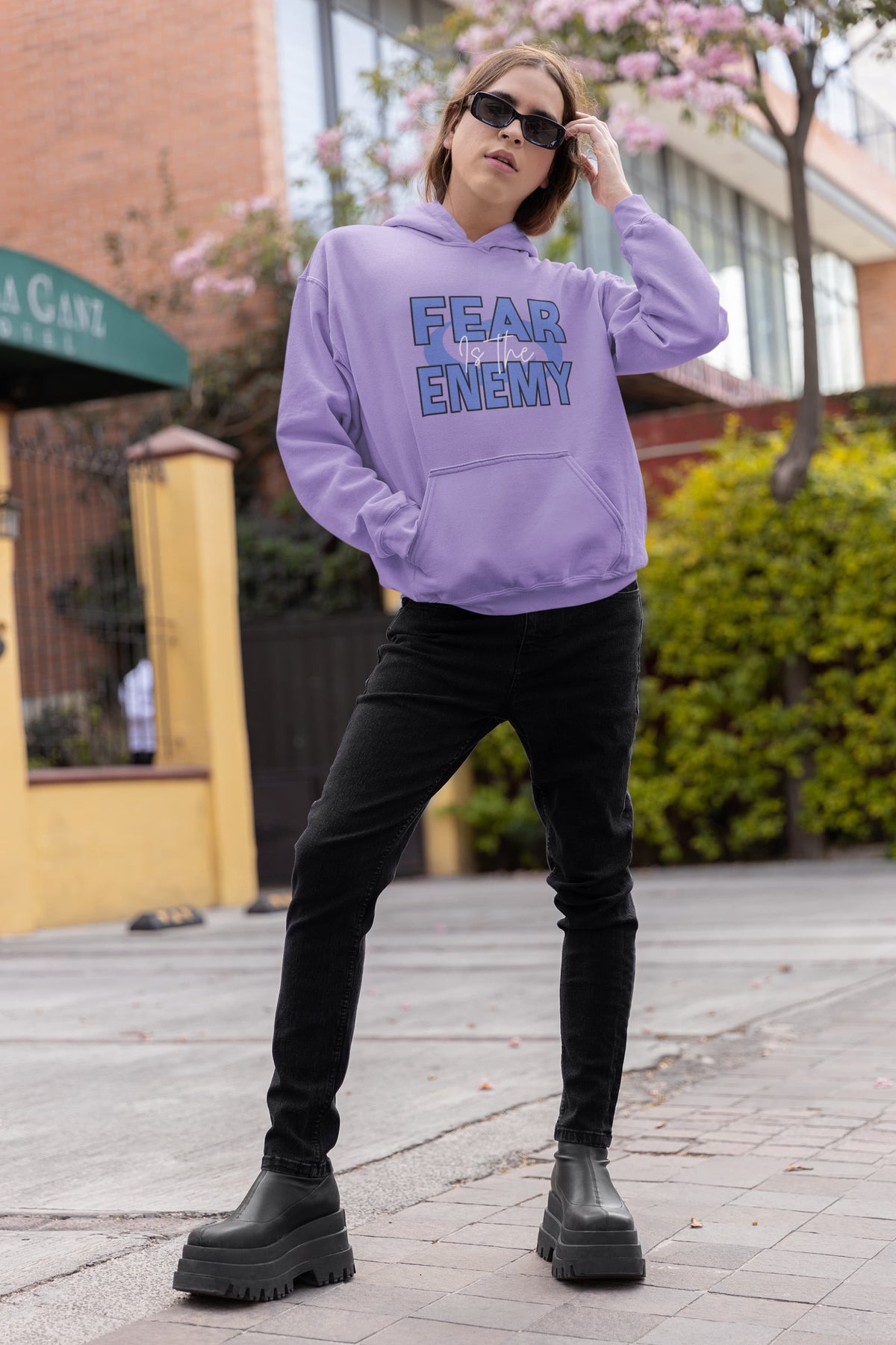 Person wearing a purple hoodie with 'FEAR NO ENEMY' text, black pants, and black shoes on a sidewalk.
