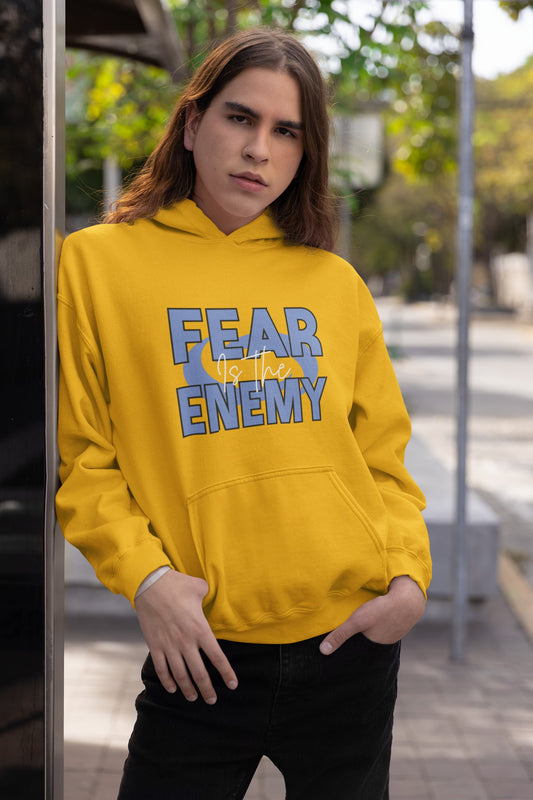 Person wearing a yellow hoodie with 'FEAR NO ENEMY' text outdoors.