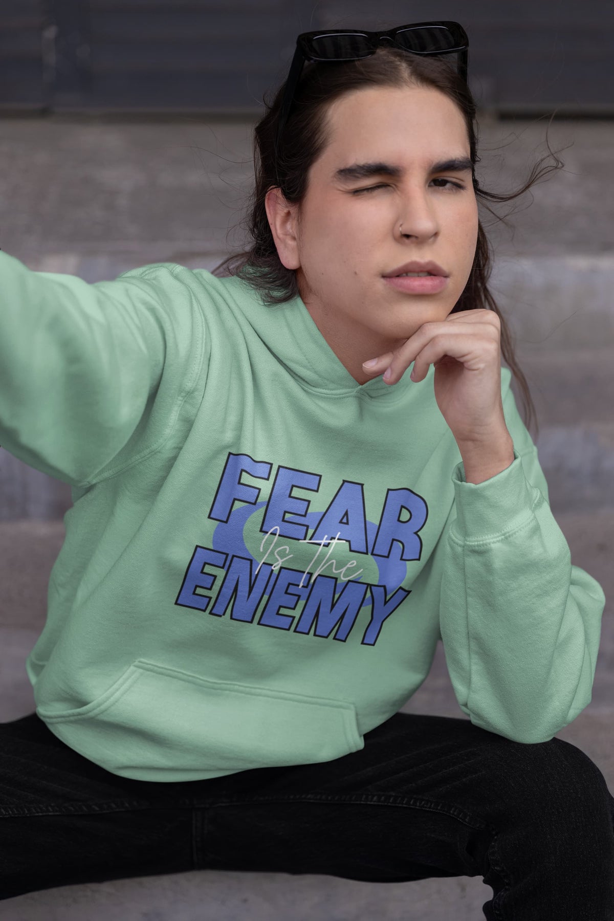 Person wearing a light green hoodie with 'FEAR THE ENEMY' text, sitting on steps.