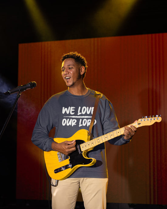 Man playing a yellow electric guitar on stage with a microphone and red curtain background