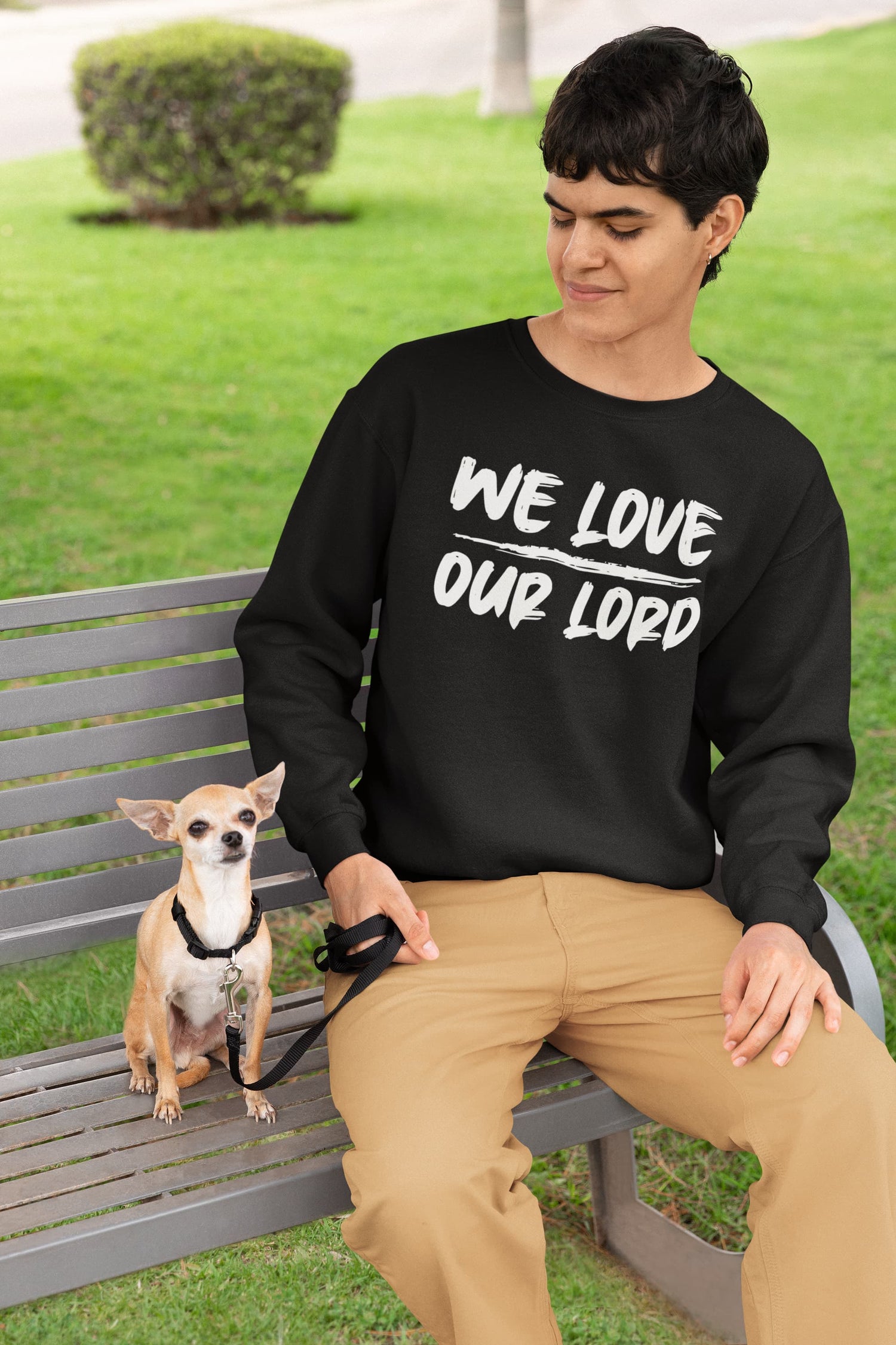 Person sitting on a bench with a dog, wearing a black sweatshirt with text, in an outdoor setting.