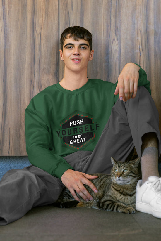 Person wearing a green sweatshirt with motivational text, sitting on the floor with a cat, against a wooden wall.