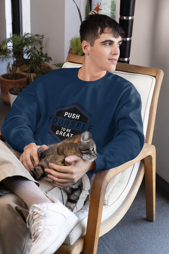 Man sitting in a chair holding a cat, wearing a blue sweatshirt with motivational text.