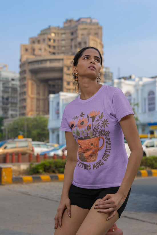 Woman wearing a purple t-shirt with a floral design and text, standing on a street with buildings in the background.