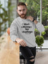 Man wearing a gray sweatshirt with text, sitting in an outdoor setting.