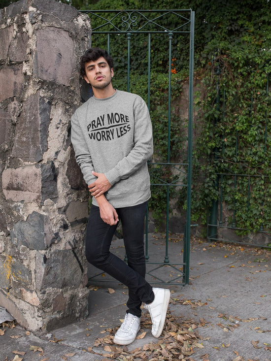 Man wearing a gray sweatshirt with text, standing against a stone wall and greenery.