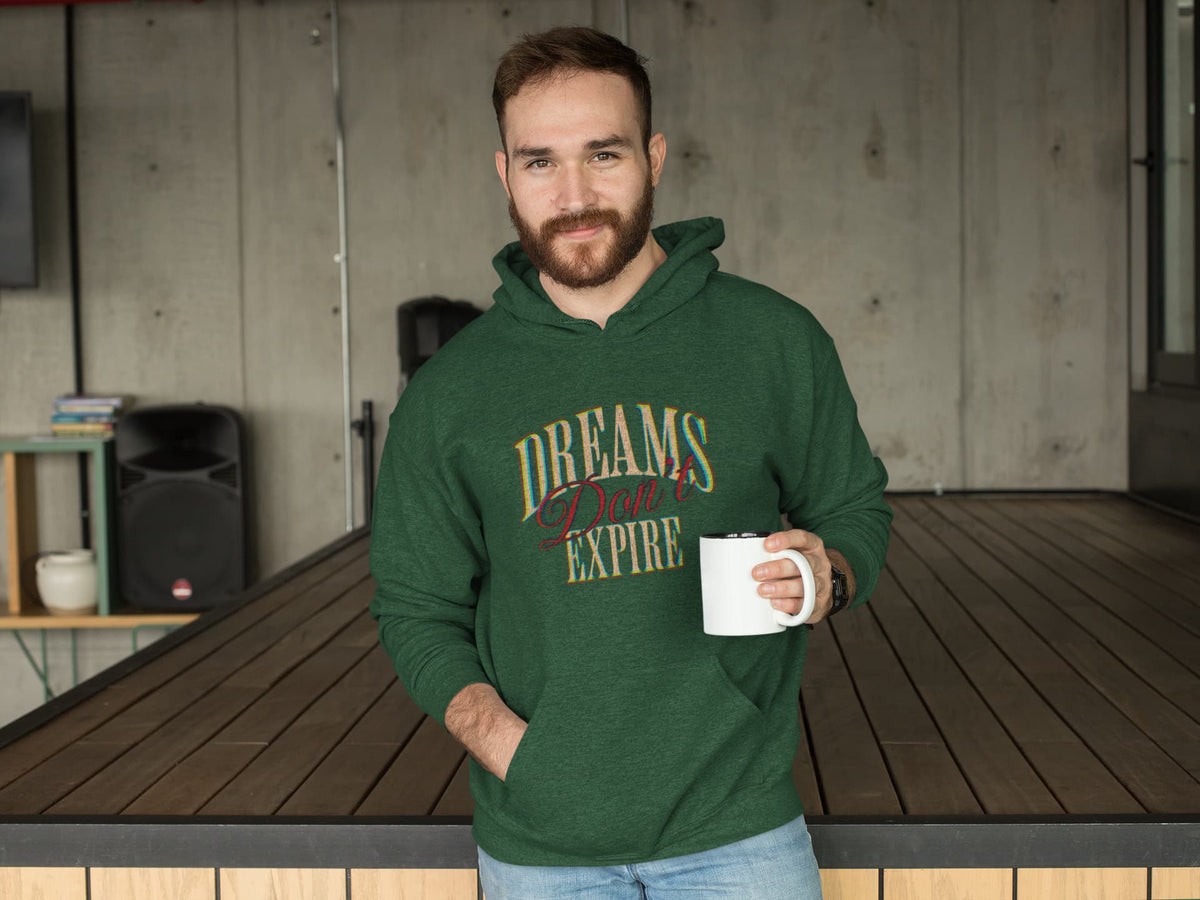 Man wearing a green hoodie with 'Dreams Don't Expire' text, holding a mug.