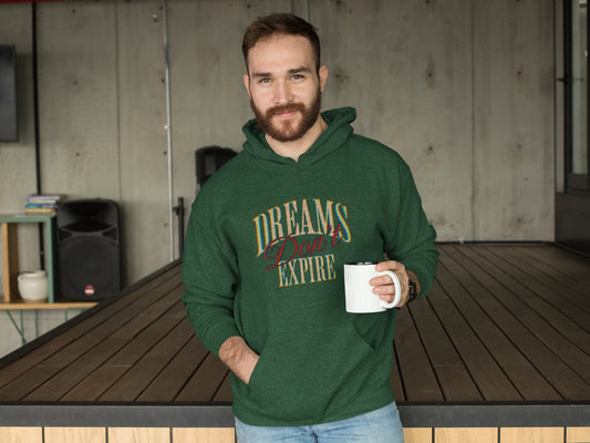 Man wearing a green hoodie with 'Dreams Don't Expire' text, holding a mug.