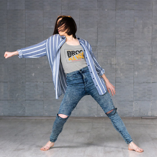 Person wearing a striped shirt and ripped jeans against a gray wall.